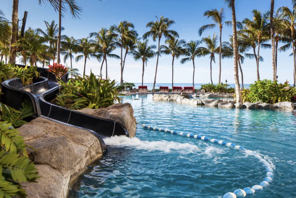 An outdoor pool surrounded by palm trees and backing on to the ocean at The Sheraton Waikiki