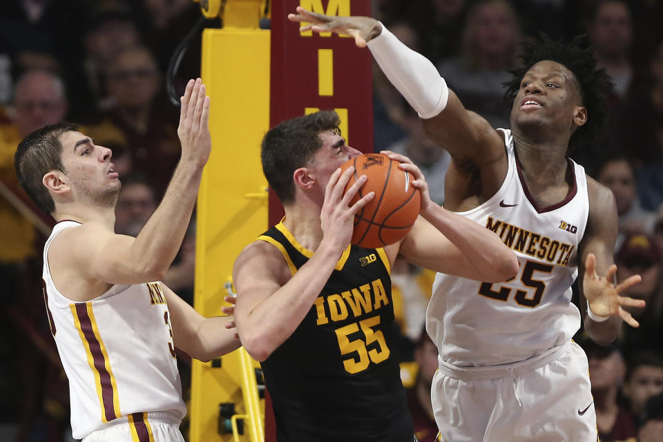 Iowa's Luka Garza (55) handles the ball against the defense of Minnesota's Alihan Demir, left, and Daniel Oturu, right, during an NCAA college basketball game Sunday, Feb. 16, 2020, in Minneapolis. (AP Photo/Stacy Bengs)