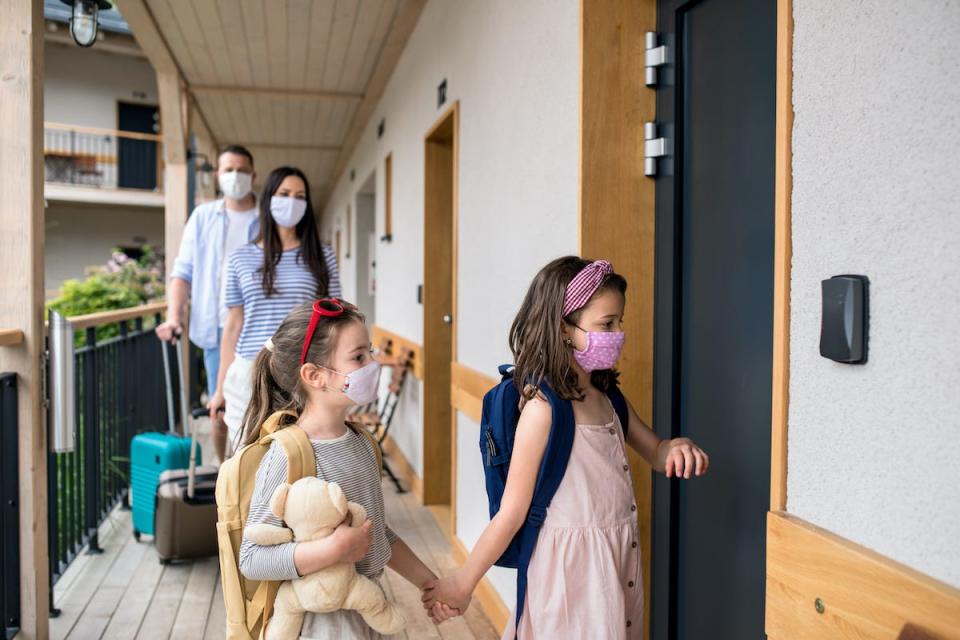 Family with children and face masks outdoors by hotel in summer, holiday concept. - stock photo