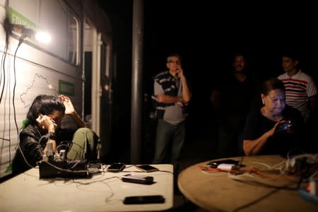 A woman uses her cell phone while charging it at a truck with an electricity generator provided by the municipality during a blackout in Caracas