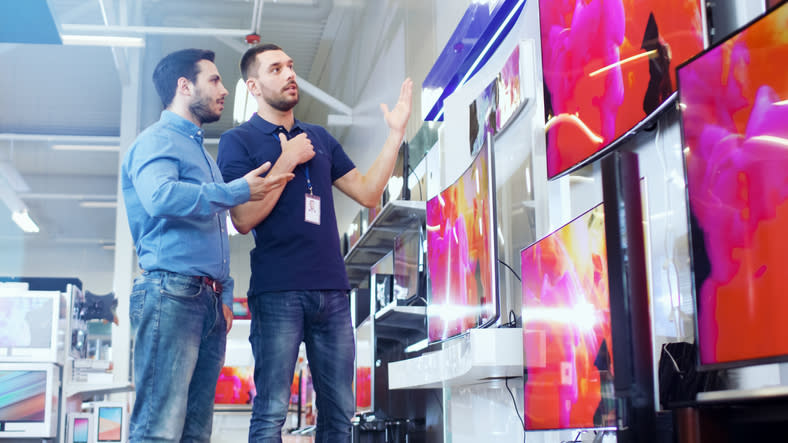 Two employees discussing TVs for sale in an electronics store