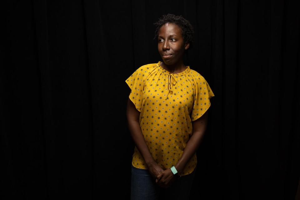 A woman stands against a black background.