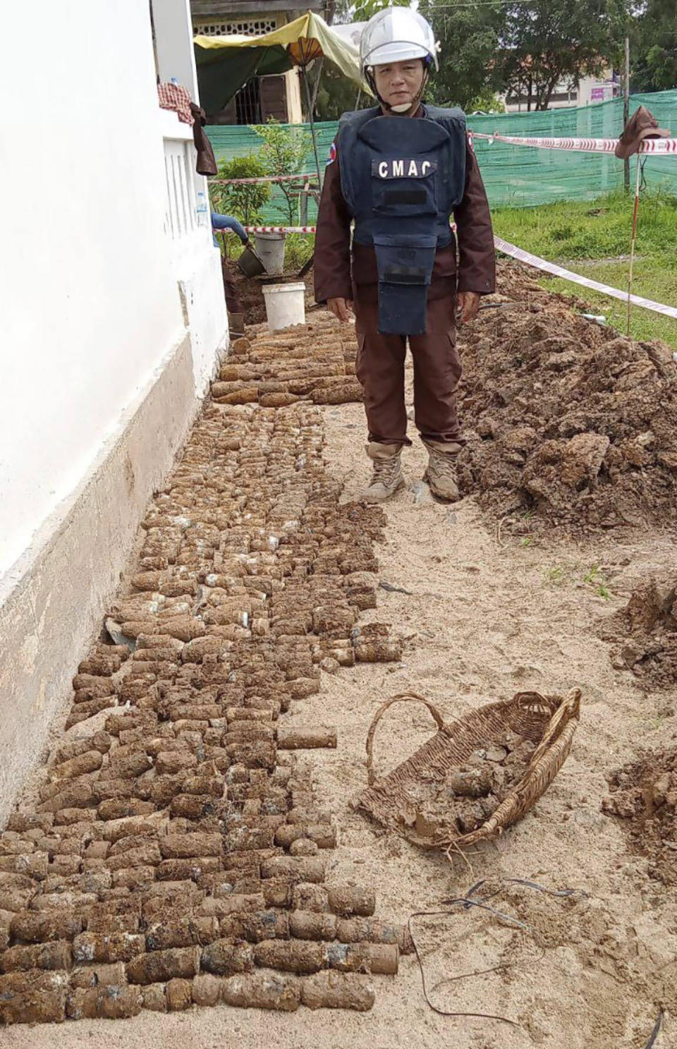 In this photo released by the Cambodia Mine Action Center, CMAC, a diminer expert stands near a pile of unexploded ordnances at Queen Kosamak Hight School in Kratie Province, northeastern of Phnom Penh, Cambodia, Sunday, Aug. 13, 2023. Cambodian authorities have temporarily closed the high school where thousands of pieces of unexploded ordinance from the country's nearly three decades of civil war have been unearthed. (Cambodia Mine Action Center via AP)