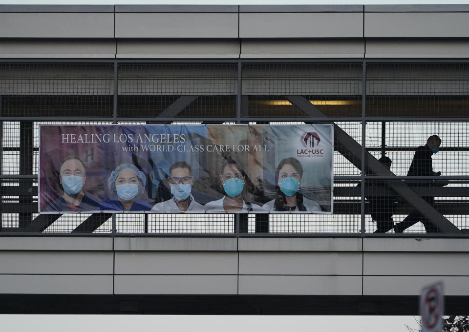 Medical personnel walk on a bridge to a hospital parking lot after their work shift at LAC+ USC Medical Center in Los Angeles, Tuesday, Jan. 5, 2021. Los Angeles continues to see hospitalizations rise day after day, setting a new record Tuesday with almost 8,000 hospitalized and more than a fifth of those in intensive care units. (AP Photo/Damian Dovarganes)