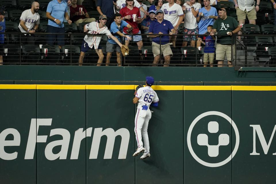 Texas Rangers left fielder Bubba Thompson leaps to the top of the wall to see a fan attempting to catch a two-run home run hit by Oakland Athletics' Elvis Andrus during the seventh inning of a baseball game in Arlington, Texas, Tuesday, Aug. 16, 2022. (AP Photo/Tony Gutierrez)