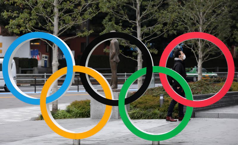 Man wearing protective face mask is seen through The Olympic rings in front of the Japan Olympics Museum in Tokyo