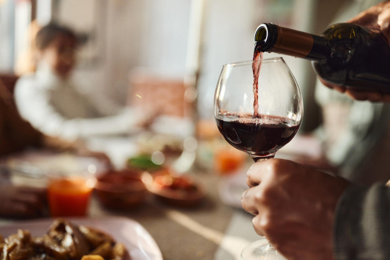 Close up of unrecognizable black man pouring red wine into a glass in dining room.