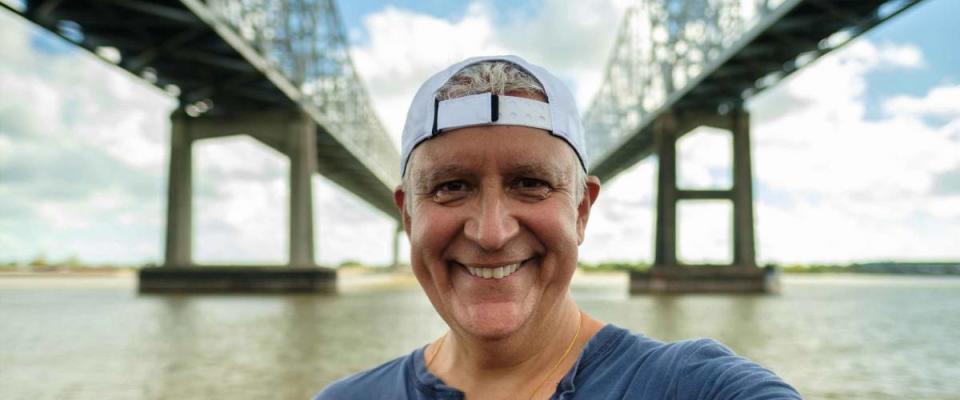 Handsome senior man taking a selfie along the Mississippi River and bridge in New Orleans, Louisiana.