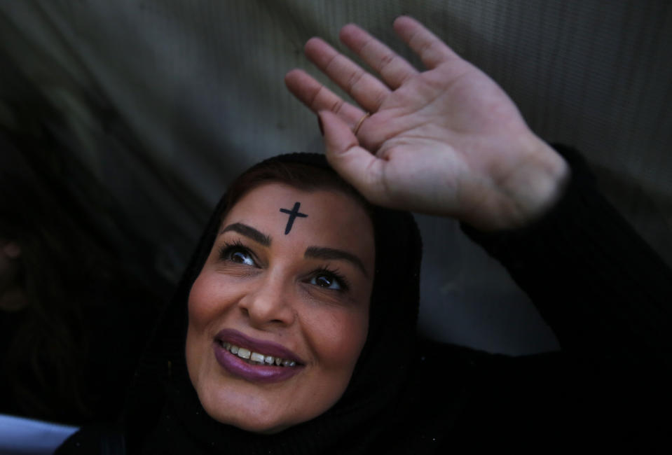 A veiled woman with a Cross on her head, waves to people that stand on their apartments balconies watching a protest at a former Beirut frontline between Christian district of Ain el-Rummaneh and a Muslim Shiite district of Shiyah, in Beirut, Lebanon, Wednesday, Nov. 27, 2019. Hundreds of Lebanese women marched across a former front line in the Lebanese capital carrying white roses and Lebanese flags to denounce overnight clashes between rival groups that injured dozens of people. (AP Photo/Hussein Malla)