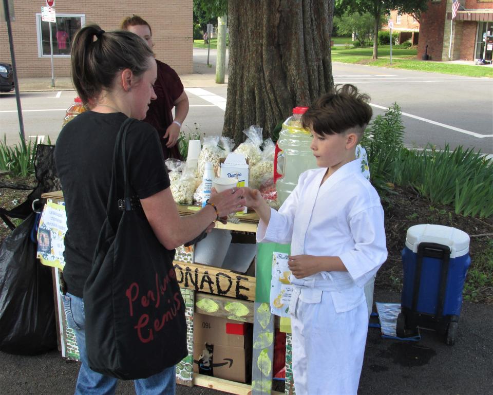 Julian Flores gives a cup of lemonade to satisfied customer Adriane Ball at Brothers Lemonade Stand outside of Local Roots on Saturday in Wooster.