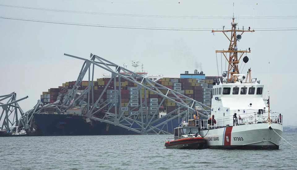 A Coast Gaurd cutter patrols in front of a cargo ship that is stuck under the part of the structure of the Francis Scott Key Bridge after the ship hit the bridge Wednesday March 27, 2024, in Baltimore, Md. (AP Photo/Steve Helber)