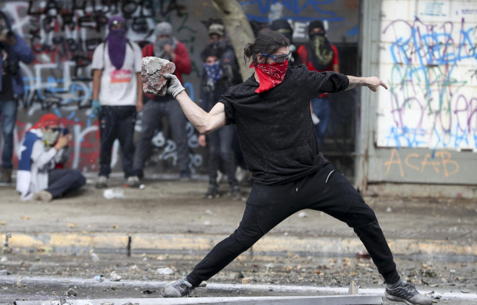 An anti-government protester throws a stone at the police during in Santiago, Chile, Monday, Nov. 4, 2019. Thousands of Chileans took to the streets again Monday to demand better social services, some clashing with police, as protesters demanded an end to economic inequality even as the government announced that weeks of demonstrations are hurting the country's economic growth. (AP Photo/Esteban Felix)