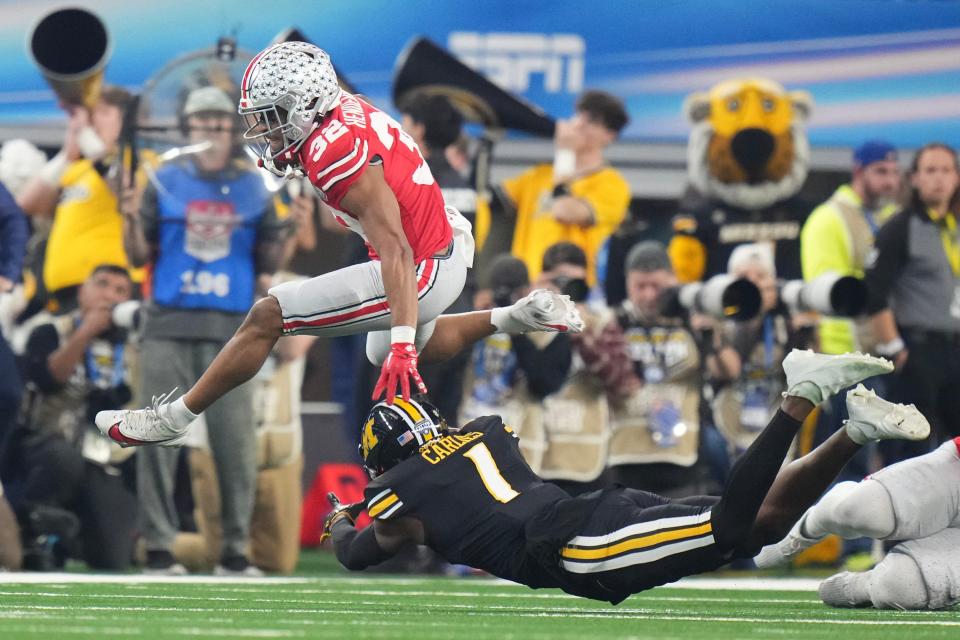 Dec 29, 2023; Arlington, Texas, USA; Ohio State Buckeyes running back TreVeyon Henderson (32) leaps over Missouri Tigers defensive back Jaylon Carlies (1) during the first quarter of the Goodyear Cotton Bowl Classic at AT&T Stadium.