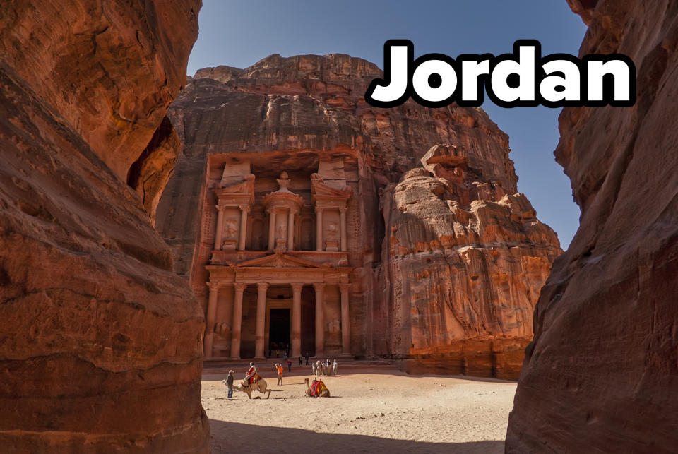 Red stone canyon path leading to Petra's treasury in Jordan, with camel sitting in front of the stone structure.