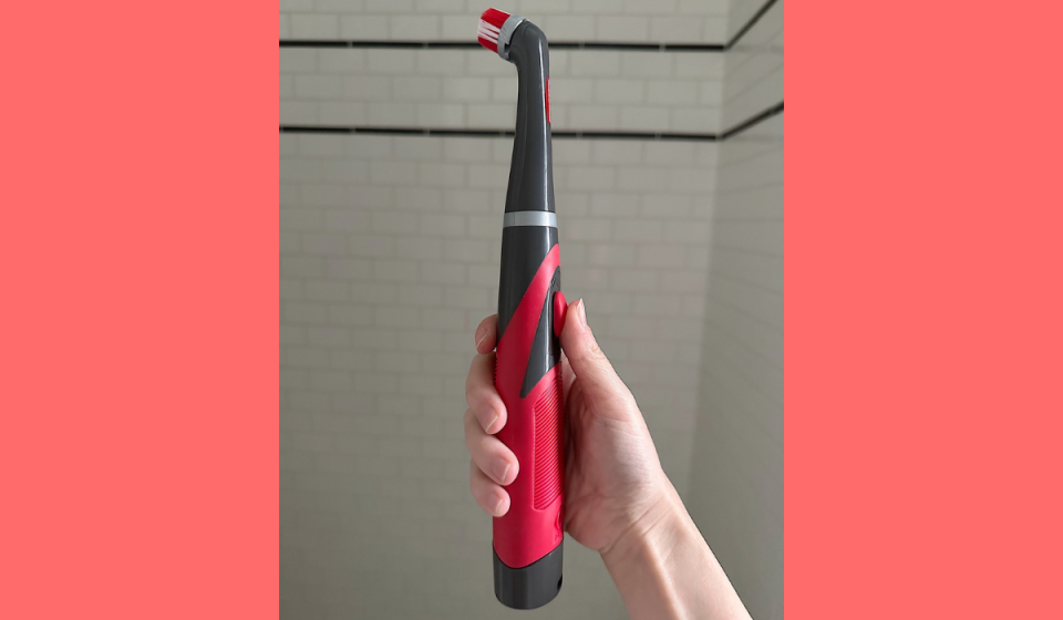 author holding the red and gray rubbermaid reveal power scrubber in front of a tiled shower