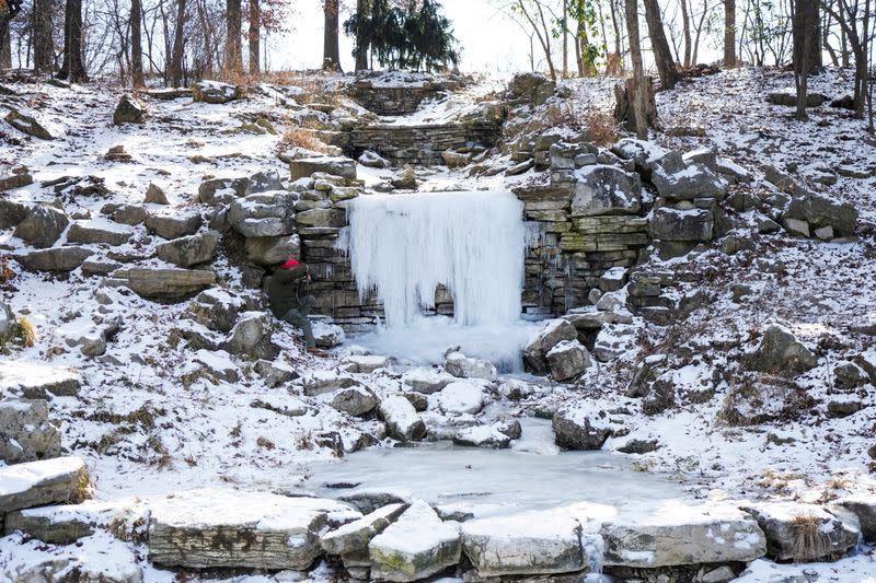 A man takes a photo of a frozen waterfall during cold weather in St Louis