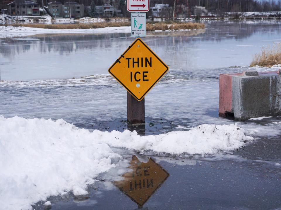 thin ice sign sits above glossy ice covered in water beside snow mound