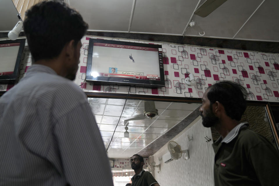 People watch a news channel airing news regarding people trapped in a cable car, at a barber shop in Lahore, Pakistan, Tuesday, Aug. 22, 2023. A cable car carrying six children and two adults dangled hundreds of meters (feet) above the ground in a remote part of Pakistan after it broke on Tuesday, trapping the occupants for hours before rescuers arrived in helicopters to try to free them. (AP Photo/K.M. Chaudary)