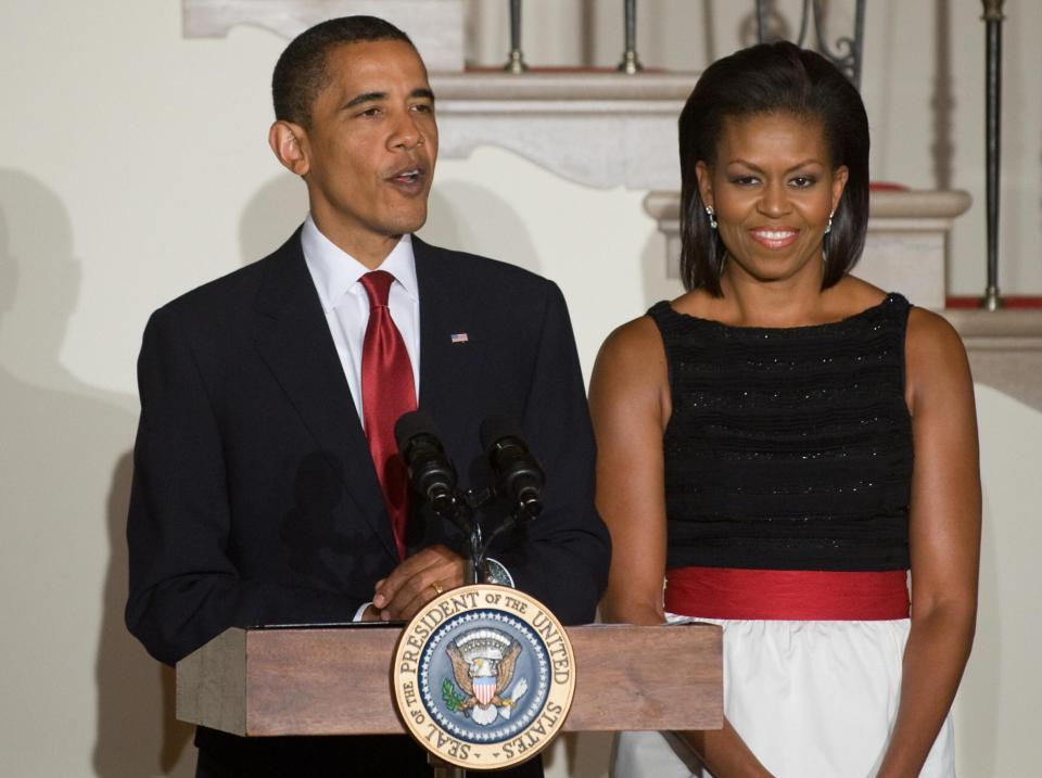 Barack Obama speaks as Michelle Obama stands behind him at an event.