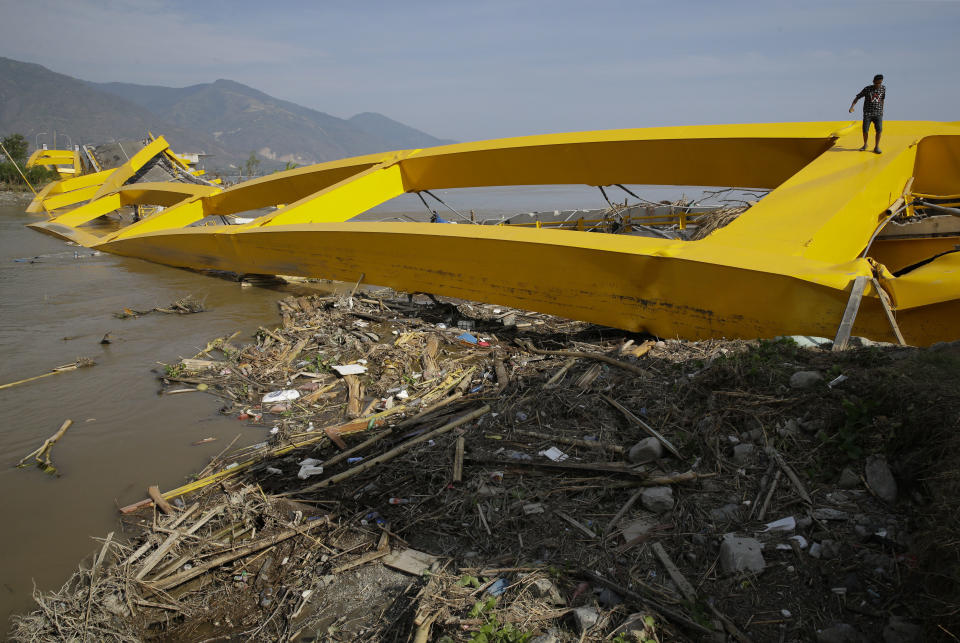 In this Oct. 4, 2018, photo, a man climbs by a bridge that was destroyed in the massive earthquake and tsunami that hit Palu, Central Sulawesi, Indonesia. Life is on hold for thousands living in tents and shelters in the Indonesian city hit by a powerful earthquake and tsunami, unsure when they'll be able to rebuild and spending hours each day often futilely trying to secure necessities such as fuel for generators. (AP Photo/Aaron Favila, File)