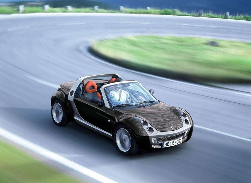 A black Smart Roadster with a red interior driving on an epic curve