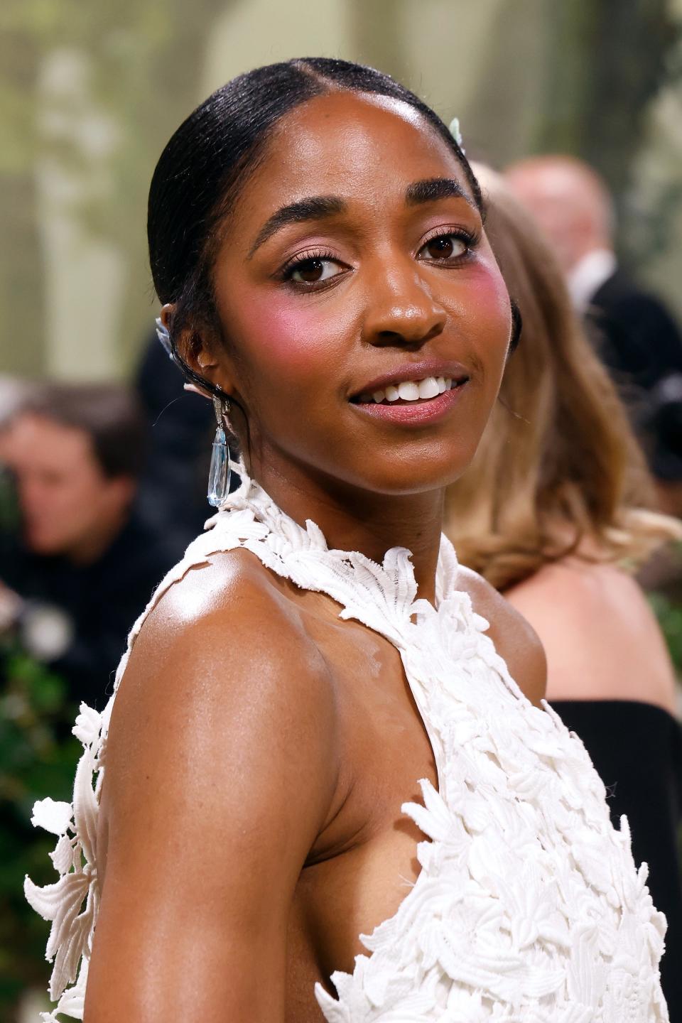 Ayo Edebiri smiling at the camera on the red carpet, wearing a textured high-neck gown