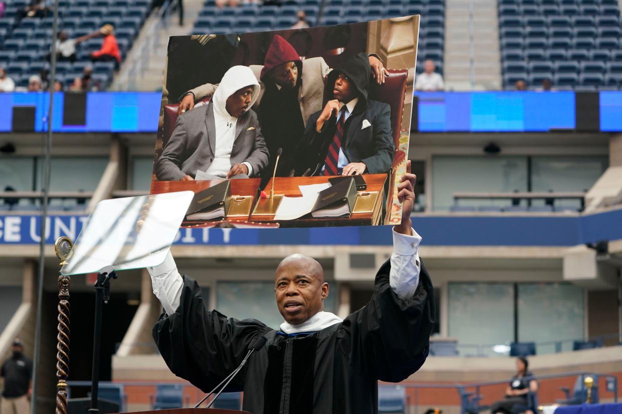 As some graduates protest New York City Mayor Eric Adams, he holds up a picture of himself protesting during his speech at a graduation ceremony for Pace University at the USTA Billie Jean King Tennis Center in Flushing, Queens, New York on Monday, May 16, 2022.