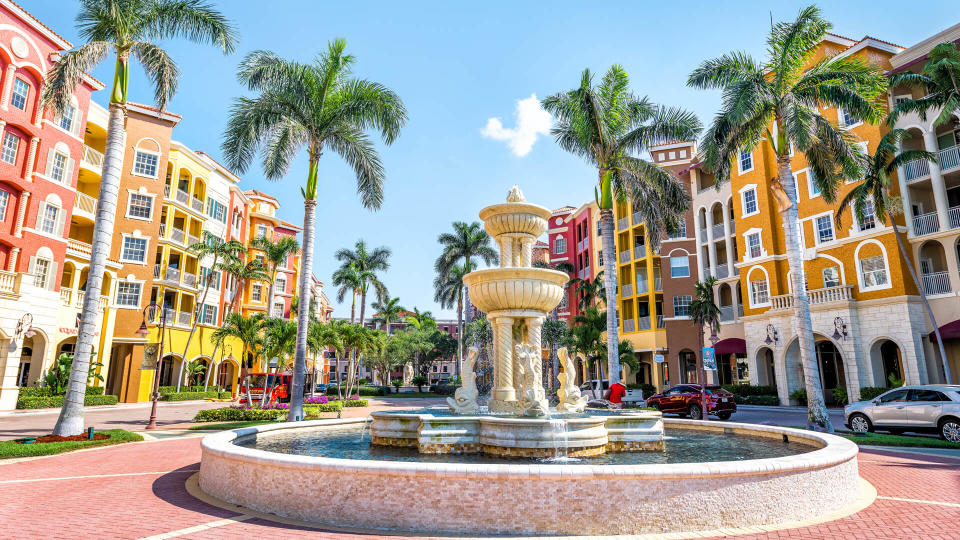 Naples, USA - April 30, 2018: Bayfront condos, condominiums colorful, multicolored, multi-colored buildings with fountain, water, palm trees, blue sky in residential community.