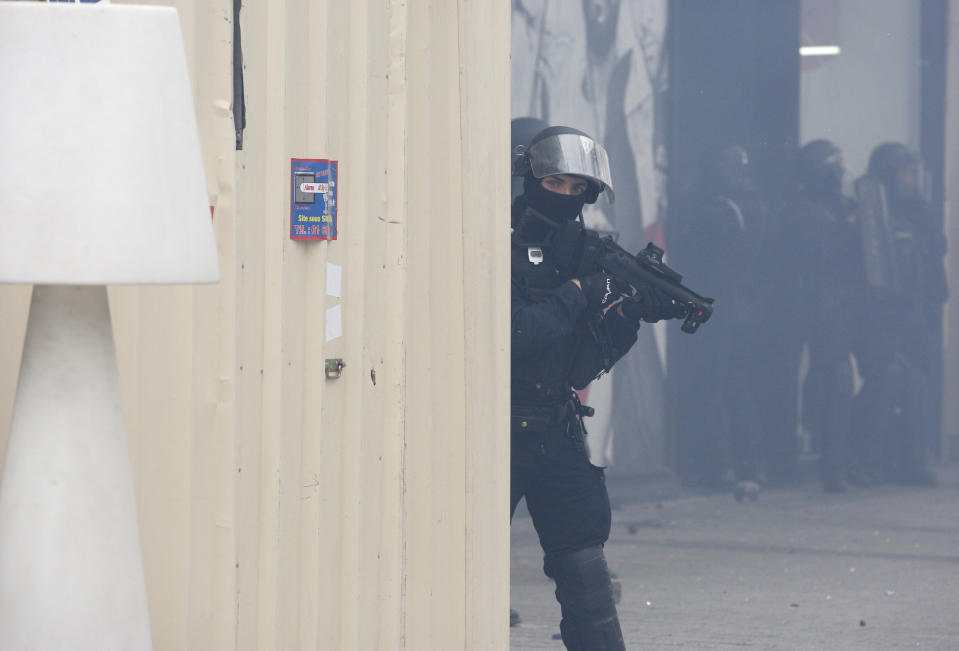 A riot police officer hides behind a fence during a yellow vests demonstration on the Champs Elysees avenue Saturday, March 16, 2019 in Paris. French yellow vest protesters clashed Saturday with riot police near the Arc de Triomphe as they kicked off their 18th straight weekend of demonstrations against President Emmanuel Macron. (AP Photo/Christophe Ena)