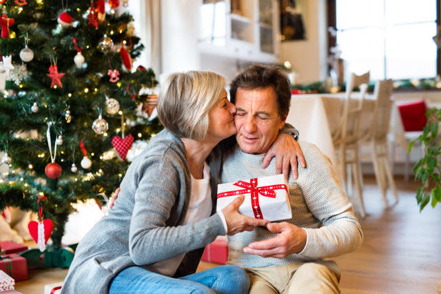 Senior couple in front of Christmas tree with presents.