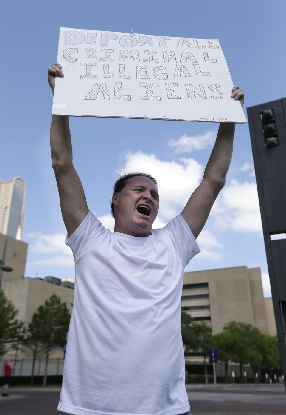 Rocky C. Beaudreau, a supporter of President Donald Trump, holds sign across the street from protestors marching through downtown Dallas, Sunday, April 9, 2017. Thousands of people are marching and rallying in downtown Dallas to call for an overhaul of the nation's immigration system and end to what organizers say is an aggressive deportation policy. (AP Photo/LM Otero)