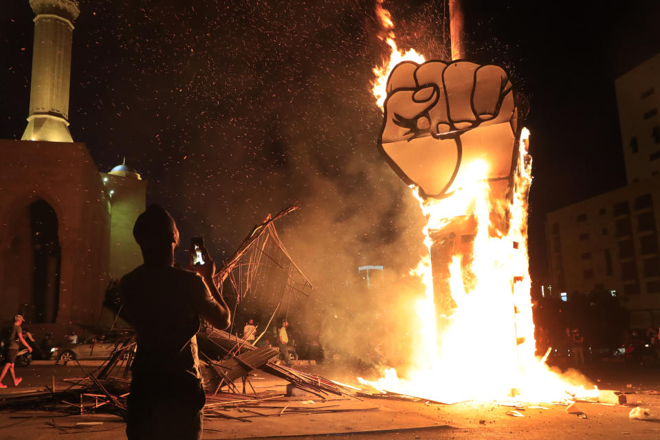 A protester takes pictures of a protest symbol that was set on fire by the supporters of former Lebanese Prime Minister Saad Hariri, after a small demonstration had denounced the naming of Hariri as a potential candidate as the country's new prime minister, in downtown Beirut, Lebanon, Wednesday, Oct. 21, 2020. Hariri resigned a year ago amid nationwide protests against government corruption and mismanagement of Lebanon's resources. (AP Photo/Hussein Malla)