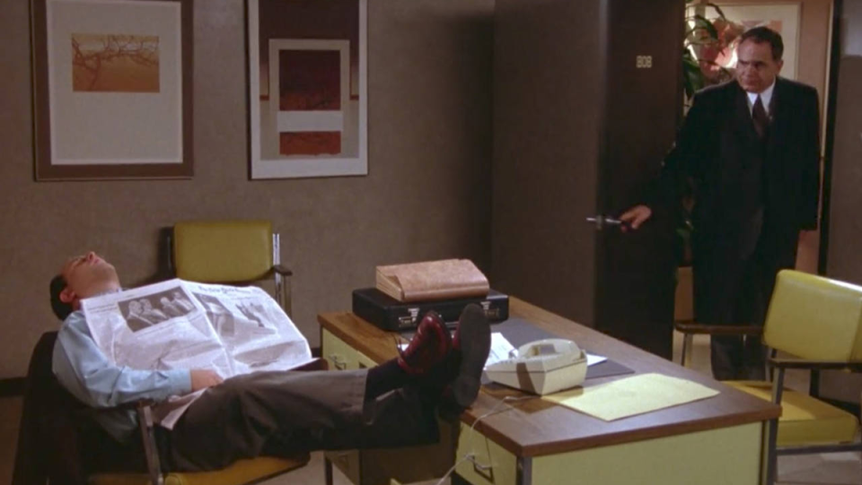 George Costanza asleep at his desk at work when his boss walks in.