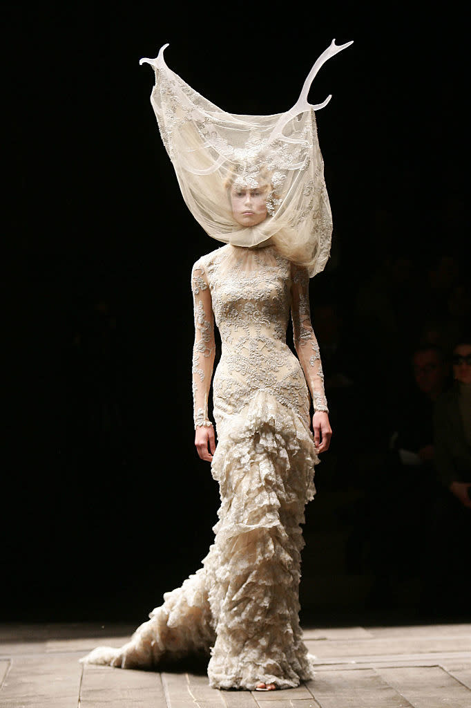 Model in ornate, textured gown with elaborate antler headpiece at fashion show