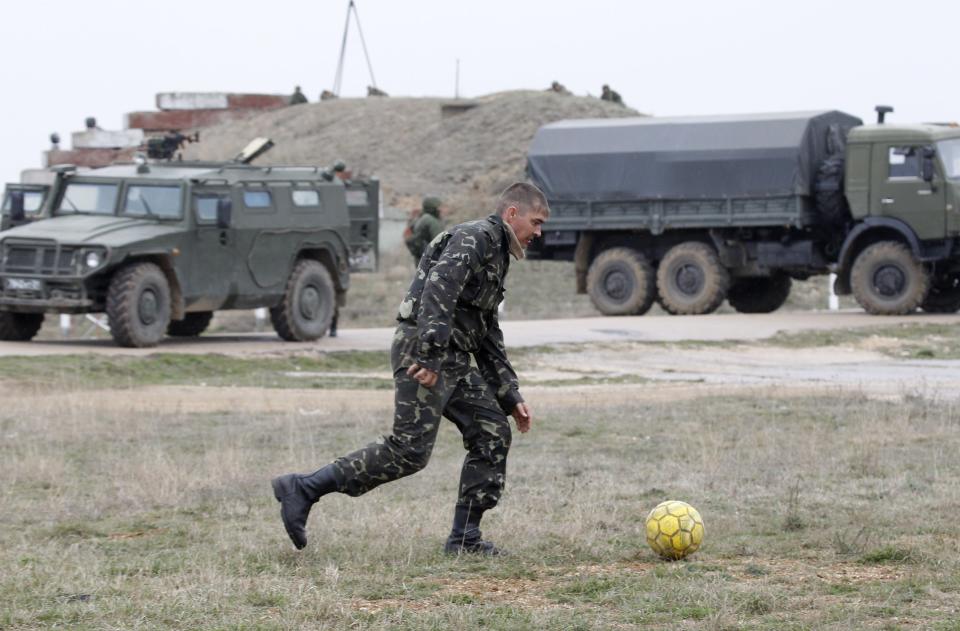 A Ukrainian serviceman kicks a football near Russian military vehicles at the Belbek airport in the Crimea region