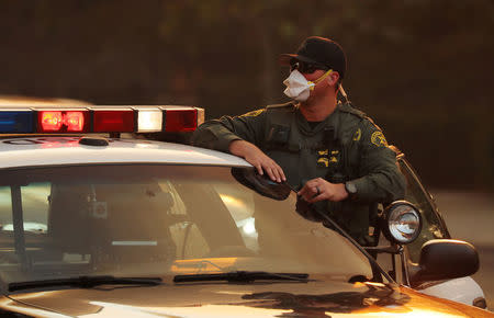 A police officer wears a mask for protection as he watches a wind driven wildfire in Orange, California, U.S., October 9, 2017. REUTERS/Mike Blake