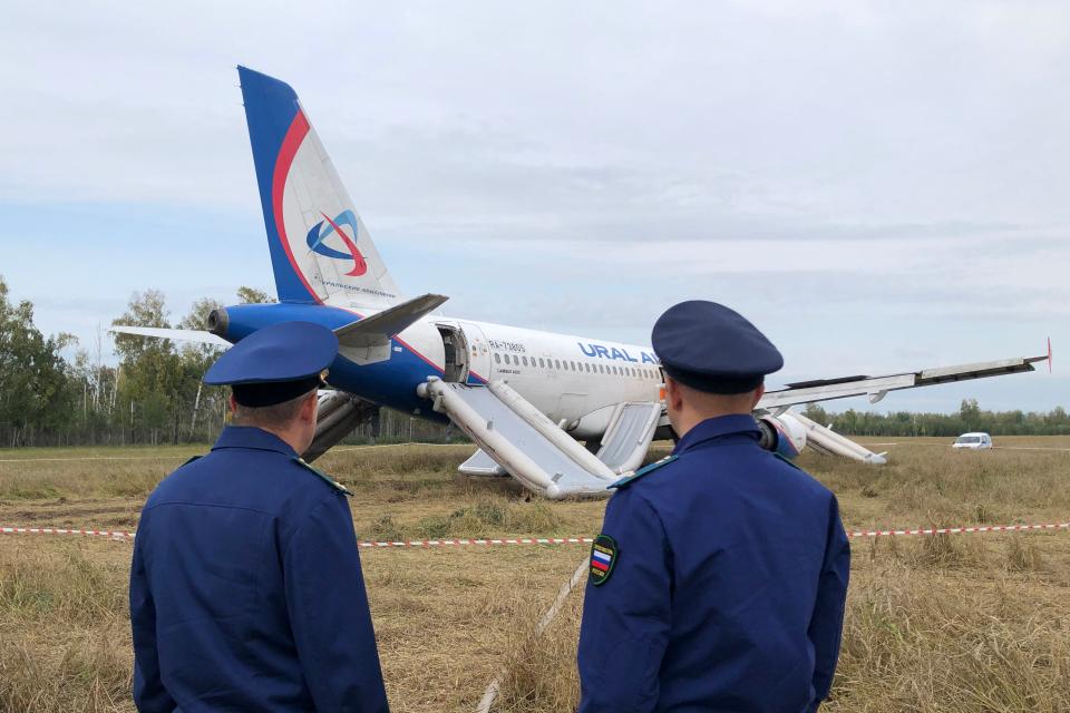 Law enforcement officers standing next to a Ural Airlines Airbus A320 passenger plane in September 2023. The plane had to make an emergency landing in an open Siberian field.