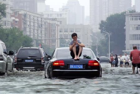 A man sits on top of a car as he is stranded on a flooded street in Tianjin, China, July 20, 2016. Picture taken July 20, 2016. REUTERS/Stringer