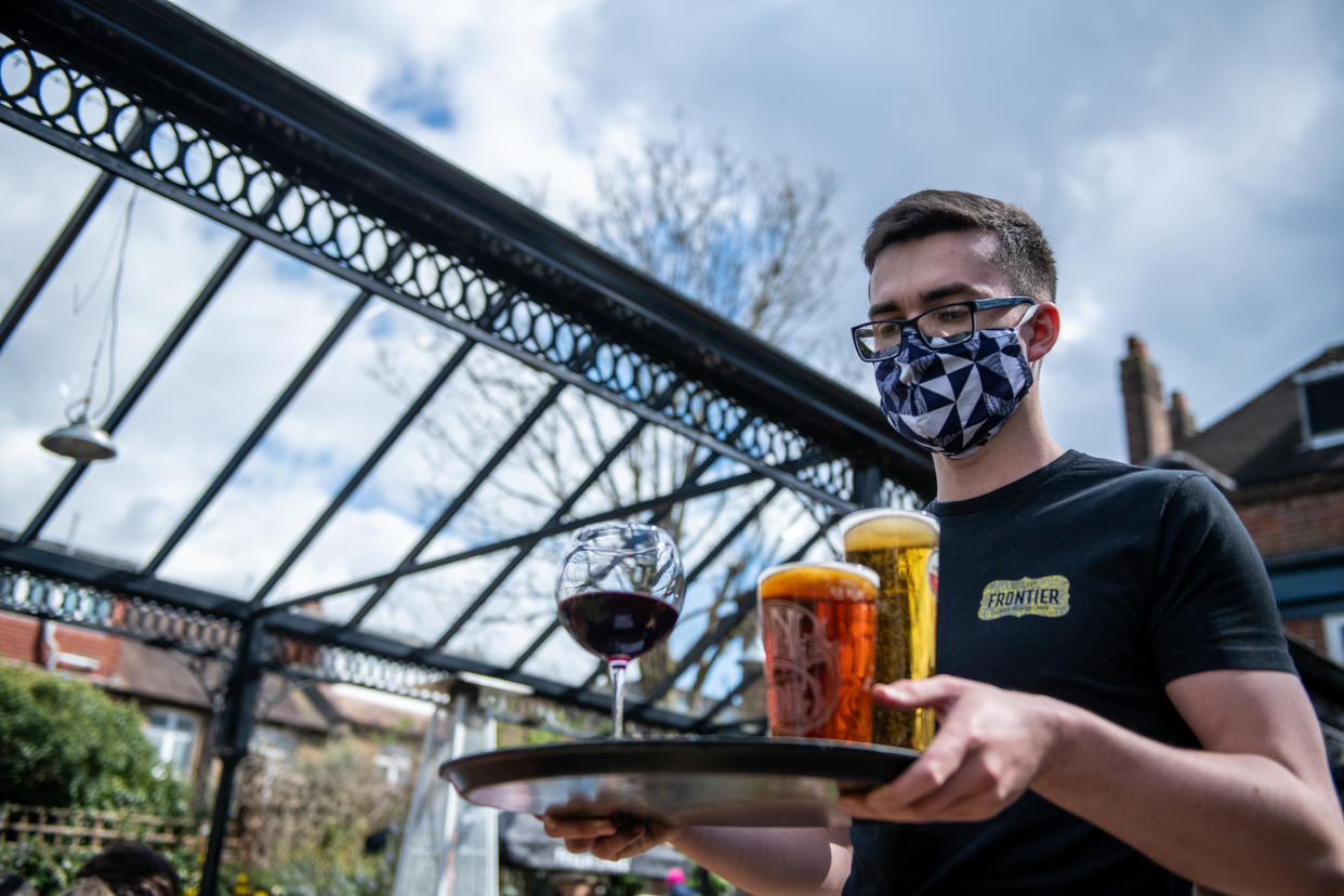 LONDON, ENGLAND - APRIL 12: Bar staff serve beer for table service in the garden of the The Duke of Kent pub which reopened at lunchtime today on April 12, 2021 in London, United Kingdom. England has taken a significant step in easing its lockdown restrictions, with non-essential retail, beauty services, gyms and outdoor entertainment venues among the businesses given the green light to re-open with coronavirus precautions in place. Pubs and restaurants are also allowed open their outdoor areas, with no requirements for patrons to order food when buying alcoholic drinks.  (Photo by Chris J Ratcliffe/Getty Images)