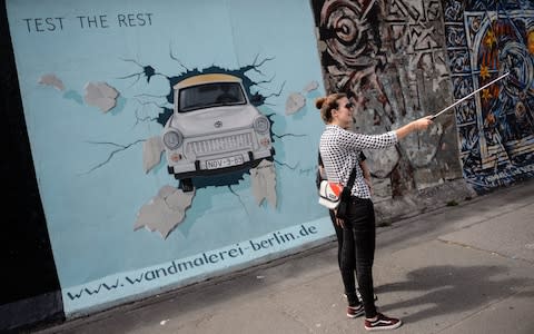 Tourists take selfies in front of the mural 'Test the Rest' by artist Birgit Kinder at a section of the former Berlin Wall called the East Side Gallery in Berlin, Germany - Credit: EPA