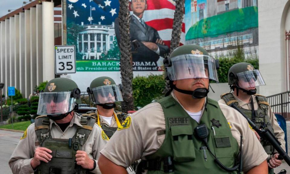 LA sheriff’s deputies stand guard as activists and relatives of Andres Guardado hold a rally near the Compton station.