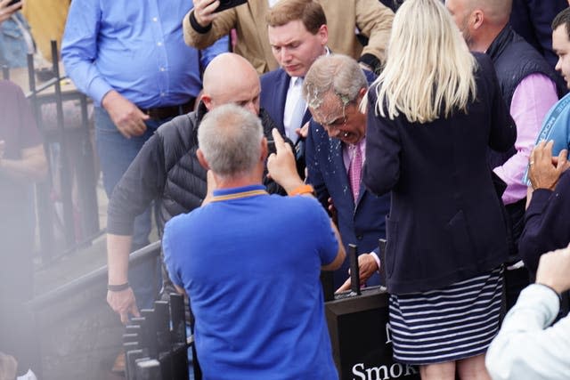 Nigel Farage surrounded by people as a milky substance drips off his bowed head