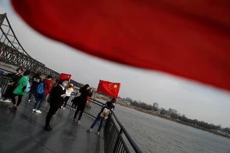 Tourists are seen taking pictures beside Chinese flags on the Broken Bridge in Dandong in China's Liaoning Province, April 1, 2017. REUTERS/Damir Sagolj/Files