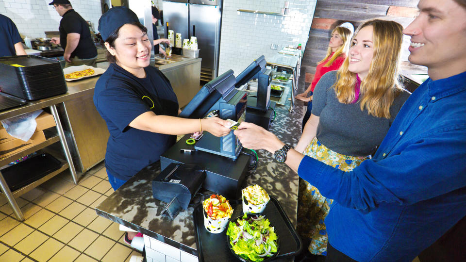 Wait staff and kitchen staff working and serving customers over the counter in a fast food restaurant.