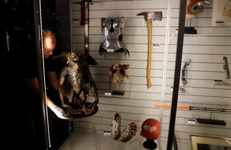 An employee of Prop Store removes from a display a Screen-Matched Mohawk Gremlin Puppet, from the film "Gremlins 2: The New Batch", at a preview of a film and tv memorabilia sale in London