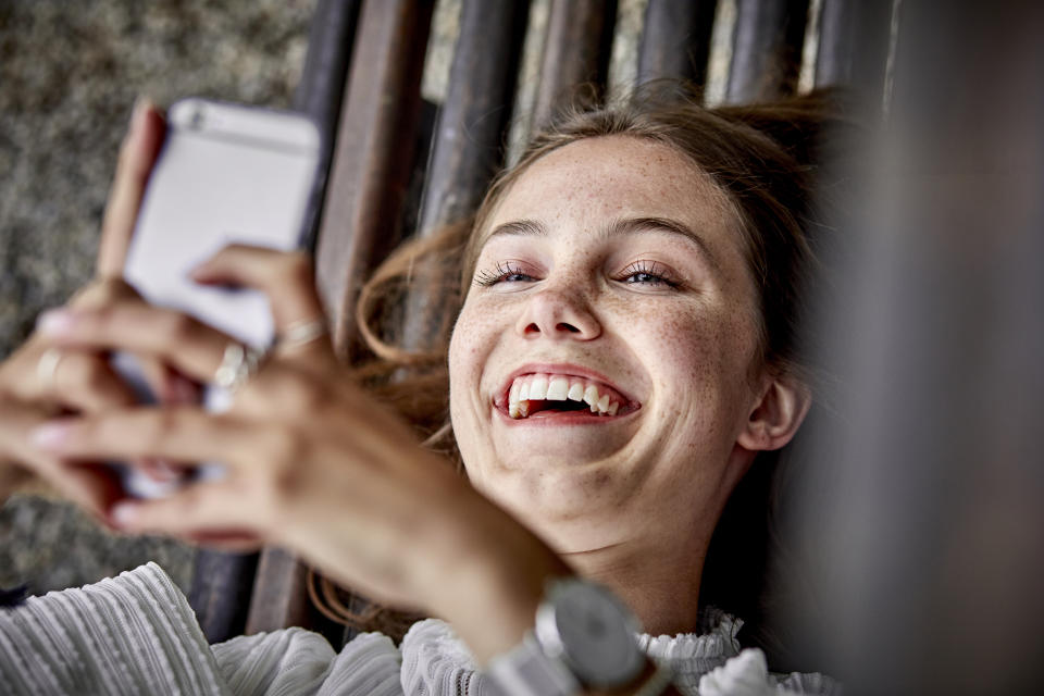 Laughing young woman lying on a bench using cell phone