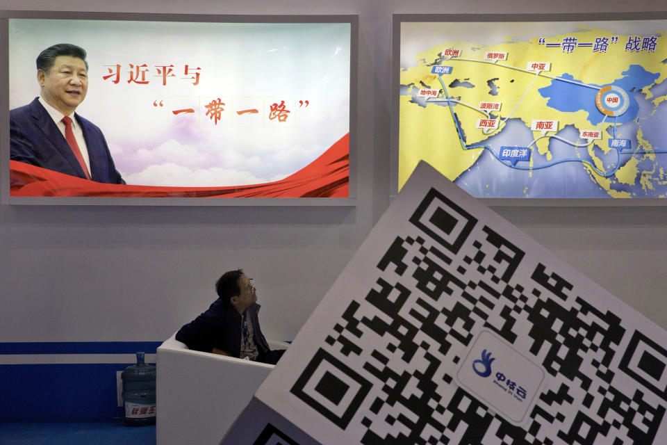 FILE - An attendee at a conference looks up near a portrait of Chinese President Xi Jinping with the words "Xi Jinping and One Belt One Road" and "One Belt One Road strategy," in Beijing, April 28, 2017. China's Belt and Road Initiative looks to become smaller and greener after a decade of big projects that boosted trade but left big debts and raised environmental concerns. (AP Photo/Ng Han Guan, File)
