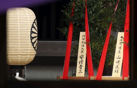 A wooden sign (L) which reads "Prime Minister Shinzo Abe" is seen on a ritual offering, a masakaki tree, from Abe to the Yasukuni Shrine, inside the main shrine as a visitor prays at the front shrine in Tokyo April 21, 2015. REUTERS/Issei Kato