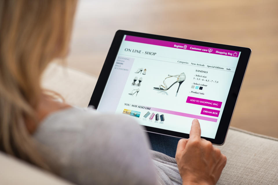 Closeup of woman doing online shopping on digital tablet at home. Rear view of woman hand touching screen while selecting shoes on ecommerce portal. Lady use e-commerce webshop to buy shoes.