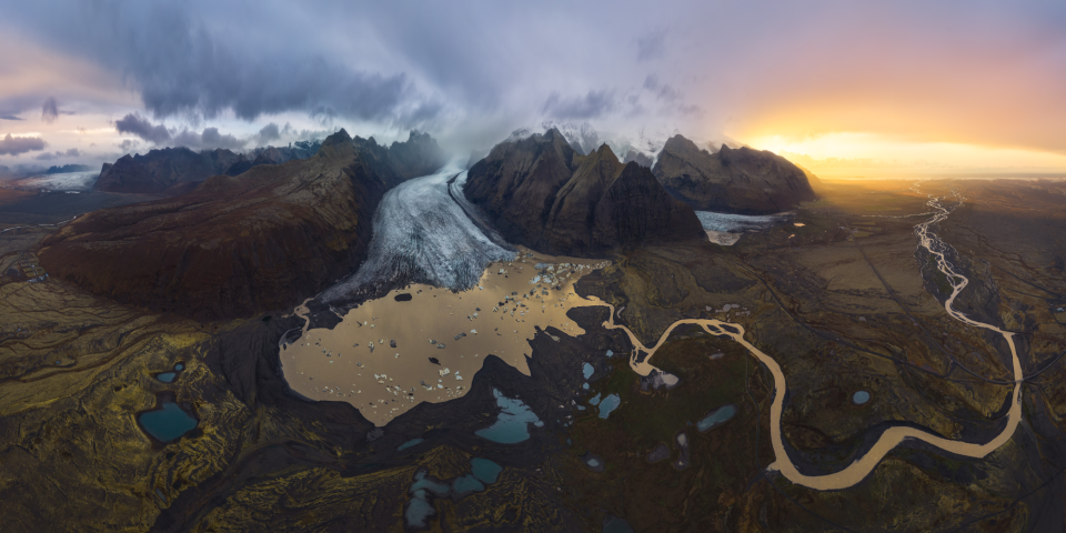 a glacier between mountains feeds into a lake and river below